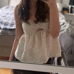 Beige broderad tubtopp - Charmig beige tubtopp med broderade blommor och en twistdetalj framtill. Toppen har en elastisk, ribbad överdel för en bekväm passform. Perfekt tröja för sommaren. 