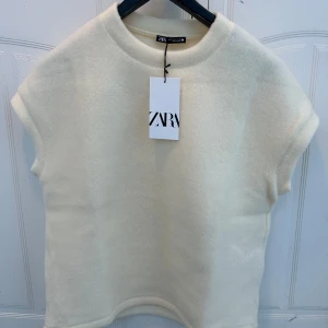 Beige kortärmad topp från Zara - Säljer en stilren beige topp från Zara med korta ärmar och rund hals. Toppen är i ett mjukt material som ger en bekväm passform. Den är helt oanvänd, endast testad och med prislapp kvar. Köptes för 300kr💞💞