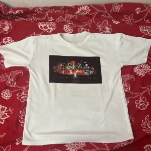 Vit Star Wars t-shirt - Säljer en vit t-shirt med ett stort Star Wars-tryck på framsidan. T-shirten är tillverkad i en blandning av bomull och polyester, vilket gör den både mjuk och hållbar. Perfekt för alla Star Wars-fans som vill visa sin kärlek till serien.