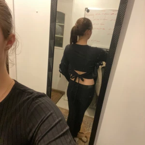 Svart ribbad topp med öppen rygg - Snygg svart ribbad topp med lång ärm och en trendig öppen rygg med knytning. Perfekt för en stilren och modern look.