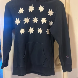Mörkblå hoodie med stjärnmönster från Champion - Säljer en mörkblå hoodie från Champion med vita stjärnor på framsidan (Limiterad). Säljer den pågrund av ingen användning. Priset kan diskuteras. 