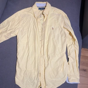 Gul skjorta från Ralph Lauren - Säljer en stilren gul skjorta från Ralph Lauren i storlek M. Skjortan är slim fit och tillverkad i 100% bomull. Den har långa ärmar och knappar framtill. En broderad logotyp i form av en polospelare finns på bröstet. Perfekt för en snygg och avslappnad look.