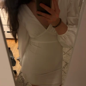 Vit långärmad klänning med v-ringning - Vit klänning med djup v-ringning och långa ärmar. Perfekt till studenten.