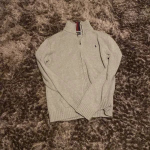Grå tröja med dragkedja från Ralph Lauren - Säljer en stilren grå tröja från Ralph Lauren med dragkedja och hög krage. Tröjan har ett diskret broderat märke på bröstet och ribbade muddar. Perfekt för en avslappnad och snygg look. Skick 9/10 inga skador, pris 500 storlek är för 170 ignorera att det står Xl för det är barn storlek. Men den är för personer runt 170-180,  pris kan diskuteras. Hör av vid fråga om storlek eller pris!
