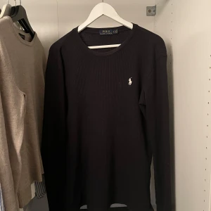 Svart långärmad tröja från Ralph Lauren - Säljer en stilren svart långärmad tröja från Ralph Lauren. Tröjan har en diskret broderad logga på bröstet och är tillverkad i ett bekvämt material. Perfekt för en klassisk och avslappnad look.