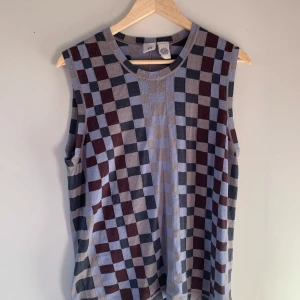 Rutig ärmlös topp från JW - Snygg ärmlös topp från JW med ett rutigt mönster i grått, blått och brunt. Perfekt för en stilren look. Toppen har en rund halsringning och är i ett mjukt material.