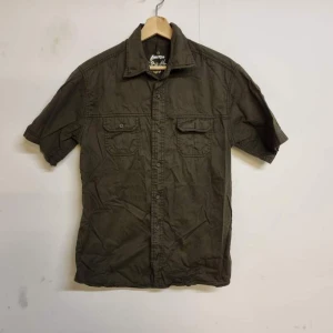 Olivgrön kortärmad skjorta från Liberto - Säljer en olivgrön kortärmad skjorta från Liberto. Skjortan har två bröstfickor med knappar och en klassisk krage. Perfekt för en avslappnad stil.