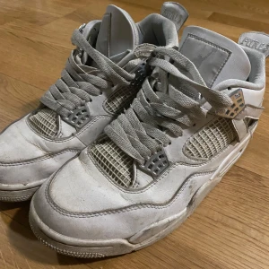 Vita Nike Air Jordans 4 - Säljer ett par vita Nike Air Jordans med klassisk design och snörning. Skorna har en ikonisk Jumpman-logga på hälen och detaljer i mesh för ventilation. Perfekta för sneaker-entusiaster!