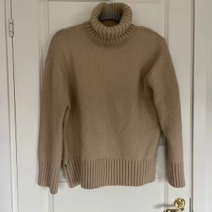 Beige stickad polotröja - Säljer en mysig beige stickad polotröja med ribbade detaljer vid krage, ärmslut och nederkant. 