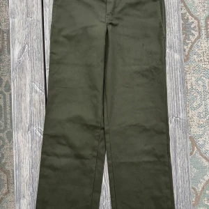 Dickies Original Work gröna - Snygga gröna byxor från Dickies i en slim straight passform. Perfekta för en stilren look med en midwaist design. Byxorna har en klassisk stil och är tillverkade i ett slitstarkt material. På vänstra låret finns skavmärken från skateboard, syns på nära håll men inte på långt. 