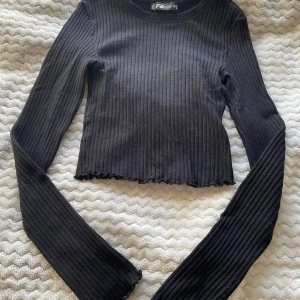 Svart ribbad tröja  - Snygg svart ribbad tröja från Newyorker i storlek XS. Tröjan är croppad med långa ärmar och har en stilren design som passar perfekt till olika outfits. Perfekt för både vardag och speciella tillfällen. Skriv gärna innan köp 😊