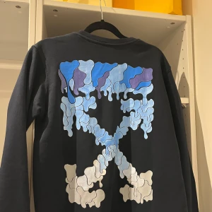 Off white tröja  - Säljer en svart långärmad tröja från Off-White med ett unikt abstrakt mönster i blått och vitt på baksidan. Framsidan har Off-White-logotypen i vitt. Perfekt för dig som gillar streetwear och vill ha något unikt i garderoben. Helt ny. S men passar M