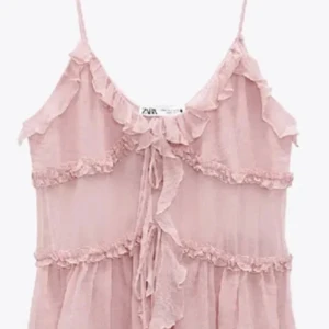 Rosa volangtopp från Zara - Söt rosa topp från Zara med volangdetaljer och knytning framtill. Den är ärmlös med tunna axelband och har en luftig design som passar perfekt för varmare dagar.