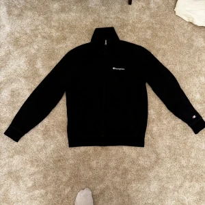 Svart fleecejacka från Champion - Säljer en svart fleecejacka från Champion med dragkedja och broderad logga på bröstet. Jackan har långa ärmar och är tillverkad i en mjuk polyesterblandning. Perfekt för kyliga dagar.  Kombinera med alla typer av kläder och den passar till nästan allt Märke: Stereotype (Zalando) Storlek :M Skick: 8/10 ord. Pris 499
