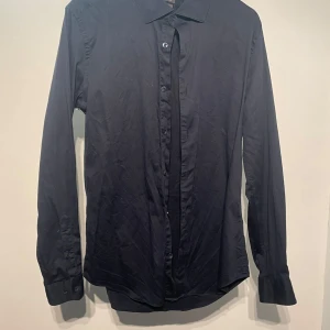 Marinblå  långärmad skjorta - Snygg marinblå långärmad skjorta med klassisk krage och knappar hela vägen ner. Perfekt för en stilren look. Passar bra till både jeans och kostymbyxor.