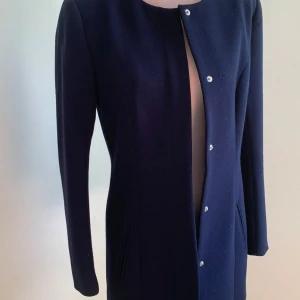 Mörkblå kappa med knappar - Elegant mörkblå kappa med stilrena knappar framtill. Den har en klassisk design med långa ärmar och diskreta fickor. Perfekt för en stilren look.