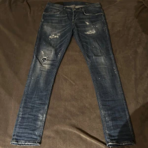 Dondup jeans storlek 33 - Säljer ett par dondups med coola slitningar och distressed detaljer. De har en klassisk femficksdesign och en knappgylf. Perfekta för en avslappnad look.