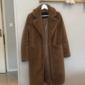 Brun teddyjacka - Mysig brun teddyjacka med långa ärmar och knappar framtill. Perfekt för kyliga dagar med sin mjuka och varma känsla. Jackan har en klassisk krage och två fickor framtill.