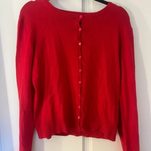 Röd kofta från H&M - Säljer en röd kofta från H&M med knappar framtill. Den har långa ärmar och en rund halsringning. 🩷
