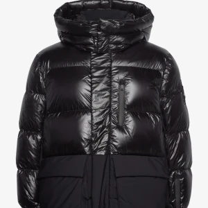 Svart moose knuckles jacka  - Snygg svart pufferjacka med glansig yta och praktisk huva. Jackan har en dragkedja framtill och flera fickor för extra förvaring. Perfekt för kyliga dagar när du vill hålla dig varm och stilren. Köpt för 11000kr mitt pris 3500kr kvitto finns kvar och den ligger kvar i original förpackningen, kan bara mötas upp 