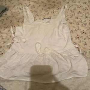 Vit linnetopp från Piazza Italia - Säljer en söt vit linnetopp från Piazza Italia i storlek S. Toppen har knytband i sidorna och en volangdetalj nedtill. Perfekt för varma sommardagar!