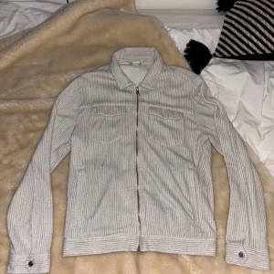 Grå ribbad vårjacka från Zara - Säljer en stilren grå ribbad jacka från Zara med dragkedja framtill. Jackan har långa ärmar och två bröstfickor med lock. Perfekt för en avslappnad look till våren. Passar med det mesta! Skriv vid några funderingar🫡 