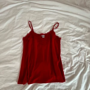 Röd linne från Amisu - Säljer ett snyggt rött linne från Amisu med spetsdetaljer vid halsringningen. Linnet har tunna axelband och är perfekt för en stilren look. Tillverkat i ett mjukt och bekvämt material.