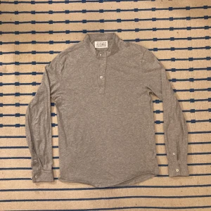 Maison Martin Margiela longsleeve-button up - Riktigt snygg Margiela tröja ifrån 2011!     Tröjan producerades under slutperioden av namnet ”Maison Martin Margiela”.   Knapparna på tröjan är utav pärlemo vilket bara det visar vilken noggrannhet som ligger bakom plagget.