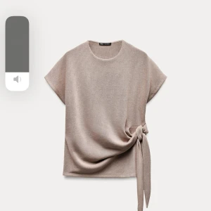 Beige topp med knyt från Zara - Snygg beige topp från Zara med rund hals och korta ärmar. Den har en elegant knytning på sidan som ger en fin detalj. Perfekt för en stilren look.