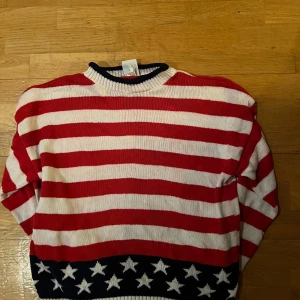 Randig tröja från Boundary Waters - Säljer en cool randig tröja från Boundary Waters i rött och vitt med stjärnmönster i blått vid nederkanten. Tröjan är långärmad och tillverkad i bomull, perfekt för en avslappnad stil. Passar bra till jeans eller shorts! En defekt på ryggen!