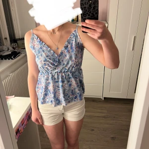 Omlottopp i blått och rosa - Söt mönstrad omlottopp i blått och rosa med smala axelband. Toppen har en v-ringad design och är perfekt för varma dagar. Stl xs men passar även s