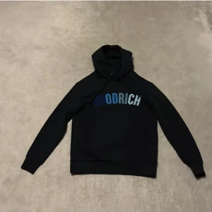 Svart hoodie från Woolrich - Snygg svart hoodie från Woolrich med blå text på bröstet. Perfekt för en avslappnad stil. Den har en klassisk huva och långa ärmar.