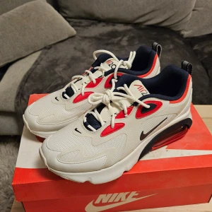 Nike AirMax 200 sneakers size 41 - Snygga Nike Air 200 sneakers i vitt med röda och navy detaljer. Skorna är helt oanvända och köpta ifrån nikes hemside. Kvitto finns. 