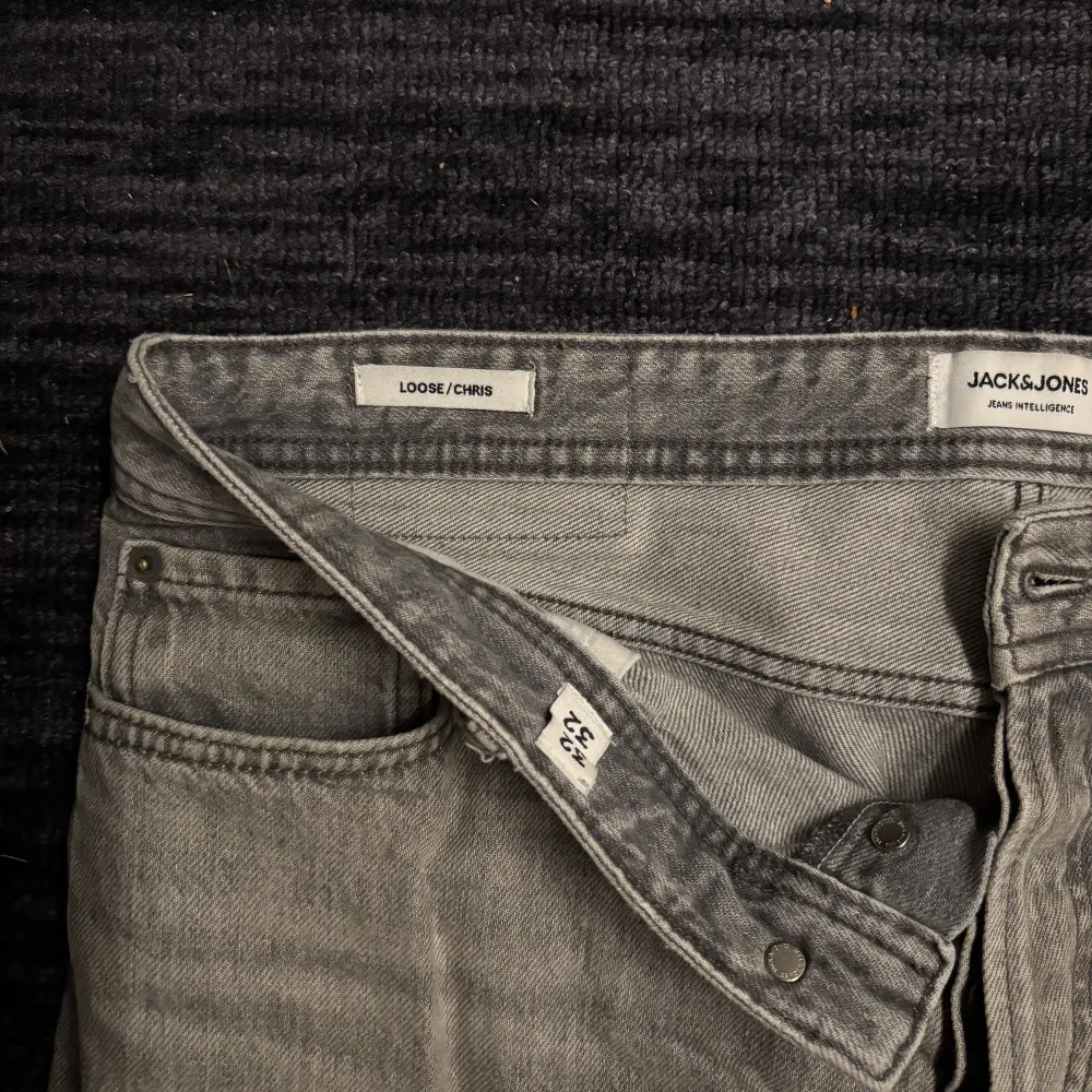 Säljer ett par grå jeans från Jack & Jones i modellen Loose/Chris. De har en avslappnad passform med klassisk femficksdesign och knappgylf. Perfekta för en casual look.. Farkut & Housut.