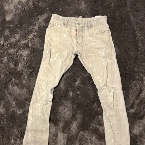 Grå jeans från Dsquared2 - Snygga grå jeans från Dsquared2 med en unik färgstänkseffekt. De har en klassisk femficksdesign och knappgylf. Perfekta för dig som vill ha en stilren men ändå iögonfallande look.