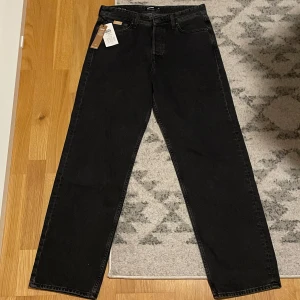 Svarta baggy jeans från Jack & Jones - Snygga svarta/mörkgråa baggy jeans från Jack & Jones i Baggy/Eddie passform, 32/34. Byxorna är aldrig använda. De har en avslappnad passform med klassisk femficksdesign och knappar i midjan. Nypris 500kr. Mitt pris 250kr