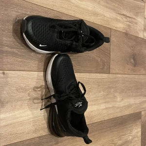 Svarta Nike sneakers - Snygga svarta Nike sneakers med vit sula och diskret logga på sidan. Skorna har snörning och en modern design som passar perfekt för både träning och vardag. Ovandelen är i syntetmaterial för bra andningsförmåga.