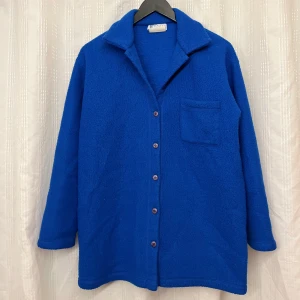 Blå fleecejacka med knappar - Säljer en mysig blå fleecejacka med knappar framtill och en bröstficka. Jackan har långa ärmar och en klassisk krage. 