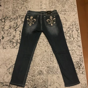 Blå jeans med leopardmönster från Miss Me - Snygga blå jeans från Miss Me med unika detaljer. De har leopardmönstrade broderier på bakfickorna och en midwaist passform. Perfekta för dig som vill sticka ut med stil! Alla stenar är kvar!!