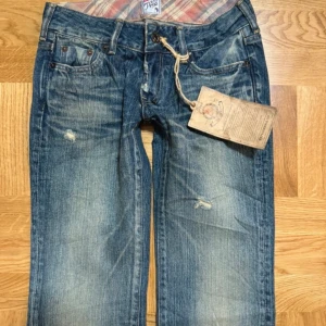 Lågmidjade bootcut jeans - Snygga blå jeans med slitningar och en vintage look. Xs-s. Midja- 34cm rakt över, midjehöjd- 17cm, innerbenslängd- 85cm.