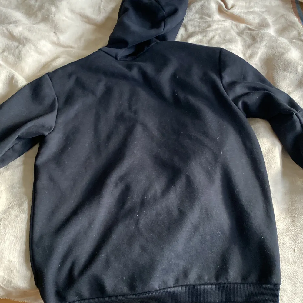 Säljer en snygg svart hoodie från Adidas med vinröda detaljer. Den har en halv dragkedja framtill och klassiska tre ränder längs ärmarna. Perfekt för höst och vinter, och den är i bra skick. Passar både för träning och vardagsbruk.. Tröjor & Koftor.