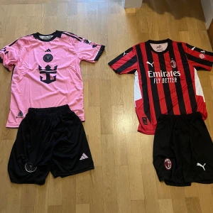 Fotbollströjor från Adidas och Puma - Säljer två fotbollströjor: en rosa kortärmad tröja med svart tryck från Adidas och en röd-svart randig kortärmad tröja från Puma. Båda tröjorna har nummer 10 på ryggen. Perfekt för fotbollsfans som vill ha något unikt i garderoben! 🏆