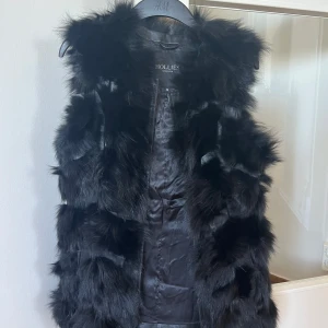 Svart pälsväst från Hollies - Säljer en elegant svart pälsväst från Hollies i storlek 38 med dragkedja. Äkta päls och använd en enda gång. Jag är ingen rökare så västen luktar inget heller. Funkar perfekt att använda till vardags eller till finare tillfällen. Funkar även för någon som bär storlek 36 beroende på hur man vill att den ska sitta. Priset går att vidare diskutera <3