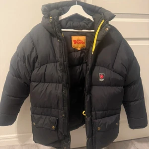 Svart dunjacka från Fjällräven - Säljer en svart dunjacka från Fjällräven.  Hätta varm och skön. Extra tjock. Har en defekt där den har blivit lappad💕 Annars i bra skick. Skriv om det är något ni undrar🥰