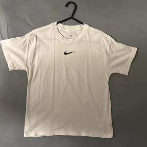 Vit t-shirt från Nike - Säljer en klassisk vit t-shirt från Nike i storlek M. Den har en broderad svart Nike-logga på bröstet och är i loose fit. Perfekt för både träning och vardag. T-shirten är i mycket bra skick och gjord av mjuk bomull.