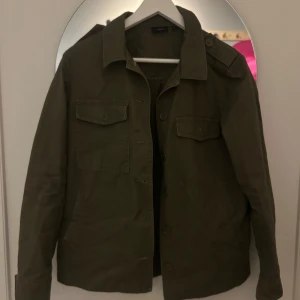 Olivgrön jacka från KappAhl - Säljer en olivgrön jacka från Kappahl i storlek S. Jackan har en klassisk design med knappar framtill och två bröstfickor. Perfekt för höst och vår, med en stilren look som passar till det mesta. Skick: mycket bra skick.