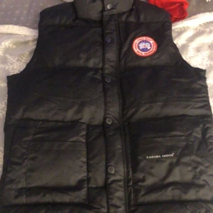 Svart dunväst Canada Goose  - Säljer en svart dunväst från Canada Goose i mycket bra skick. Västen har en hög krage och knappar framtill. Perfekt för kyliga höst- och vinterdagar. Den har också praktiska fickor och en broderad logga på bröstet. Passar både till vardags och lite finare tillfällen.