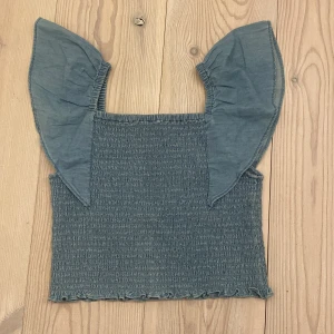 Blå topp från Kappahl - Säljer en söt blå topp från Kappahl i storlek 146/152. Toppen har en smockad design och volang ärmar! Den är ljusblå och har en lite jeans aktig känsla!💕 Inga hål eller defekter, och använt fåtal gånger! 