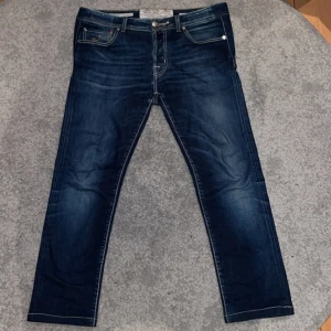 Mörkblå jeans från Jacob Cohen - Säljer ett par snygga mörkblå jeans från Jacob Cohen. De har en klassisk femficksdesign och en snygg tvätt som ger en cool look. Jeansen har en knappgylf och en läderpatch med logga baktill. Perfekta för både vardag och fest! Skavanker förekommer som Jacob Cohen märket i bak samt lilla slitningen inringad på sista bilden men annars i fint skick🙌🏻 vid frågor och funderingar skriv gärna!                                                                                                 Mvh Doré.reselll