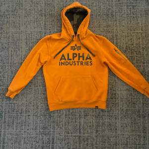 Säljer en snygg orange hoodie från Alpha Industries i storlek S. Den har en stor logga på framsidan. Perfekt för höst och vår med sin mjuka och bekväma passform. Huvan har justerbara snören för extra komfort. Passar både till vardags och chillkvällar. 🧡